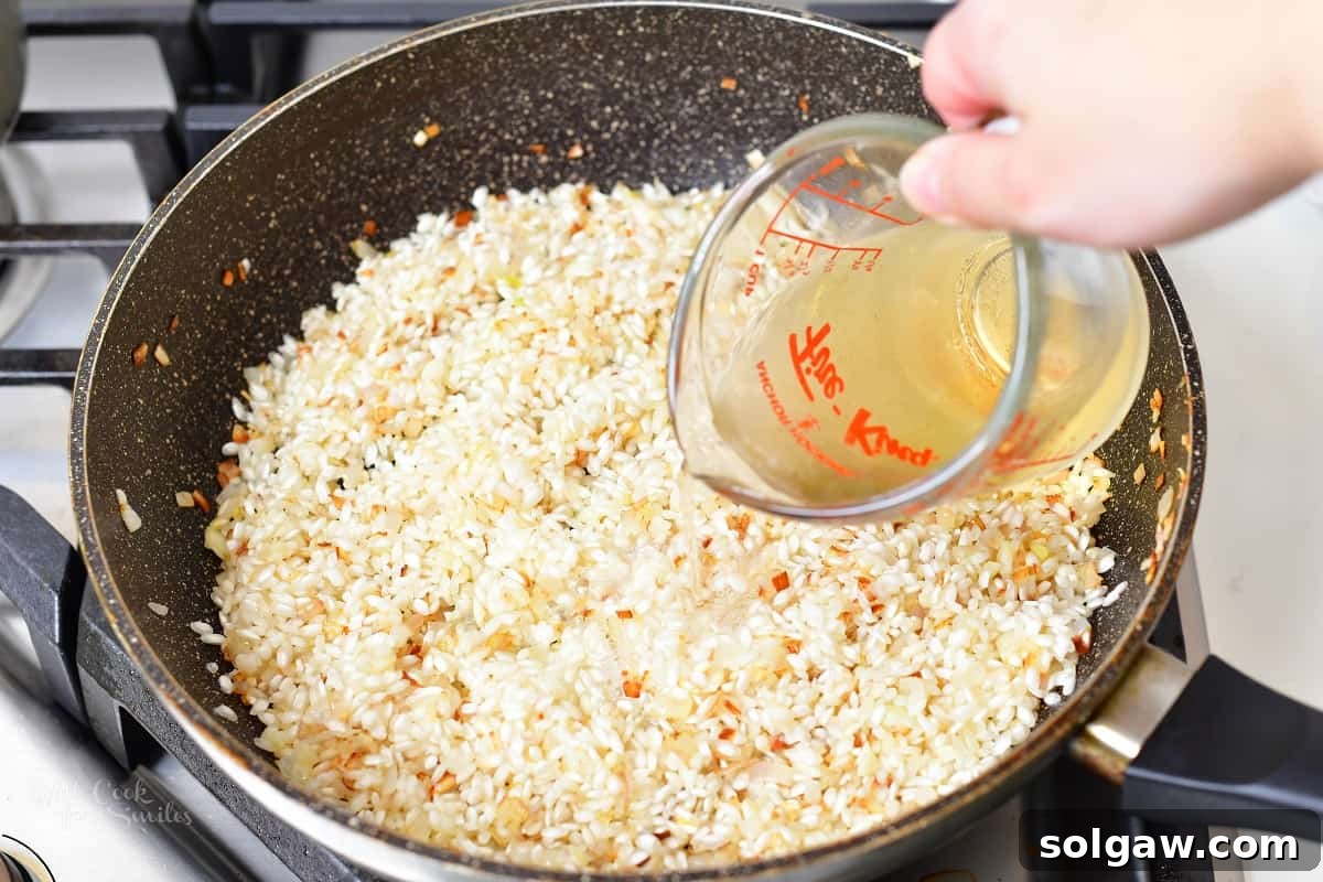Arborio rice stirred into the fragrant shallot and garlic mixture in a pan, toasting slightly before liquid is added.