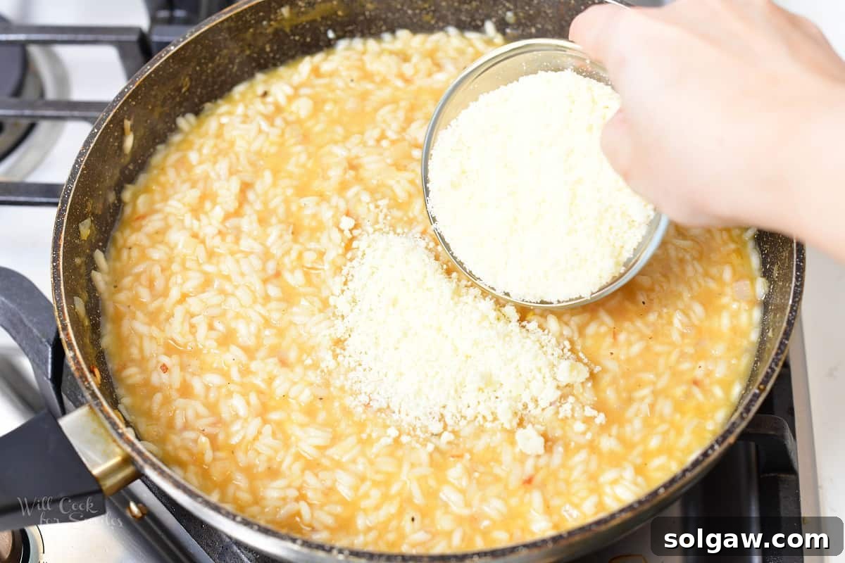 A ladle of warm chicken stock being added to Arborio rice in a pan, a crucial step for achieving creamy risotto.