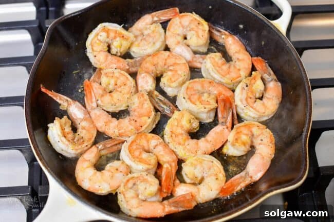 Several pieces of lemon pepper shrimp searing in a cast iron skillet, turning pink and opaque.