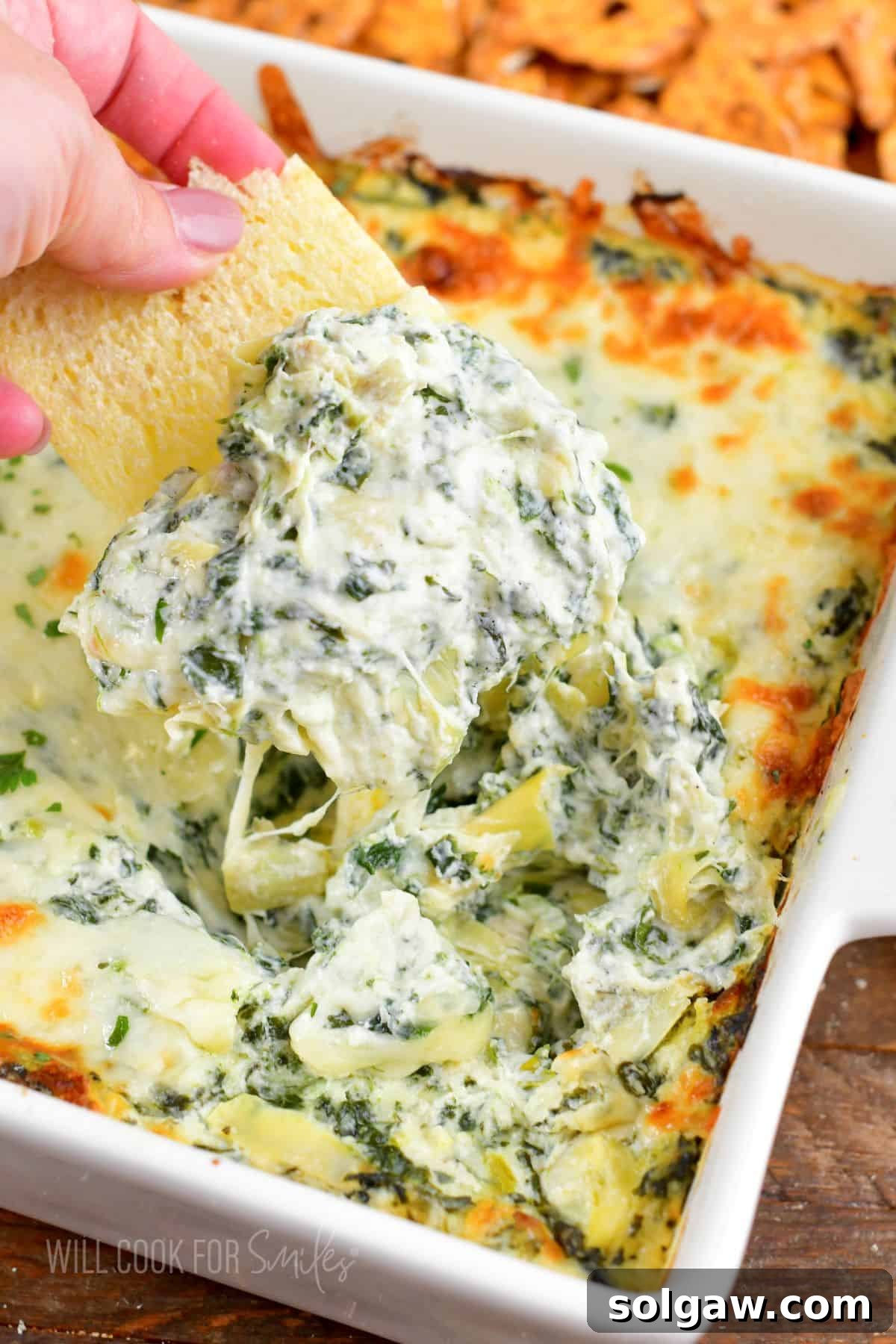 A cracker scooping up some creamy spinach artichoke dip, showcasing its cheesy texture and inviting warmth.