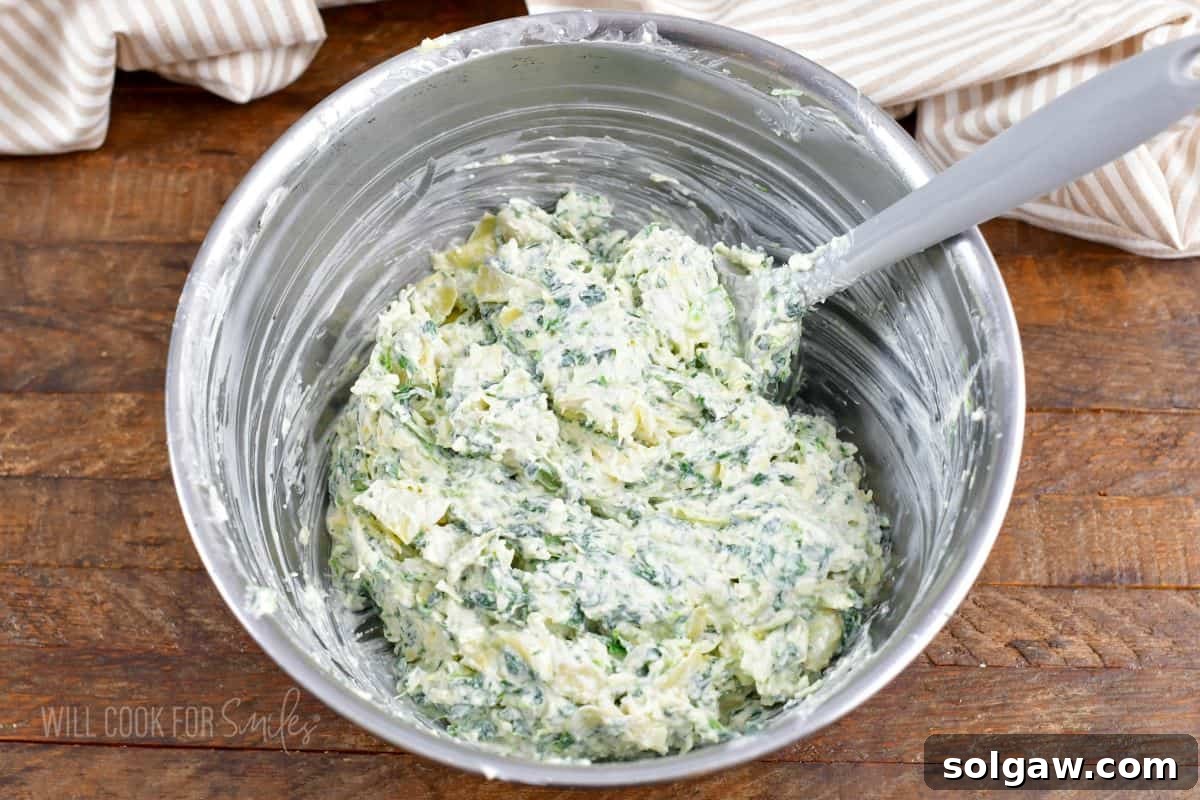 All the spinach artichoke dip ingredients thoroughly mixed together in a bowl, forming a creamy, chunky mixture, perfectly ready for transfer to a baking dish.