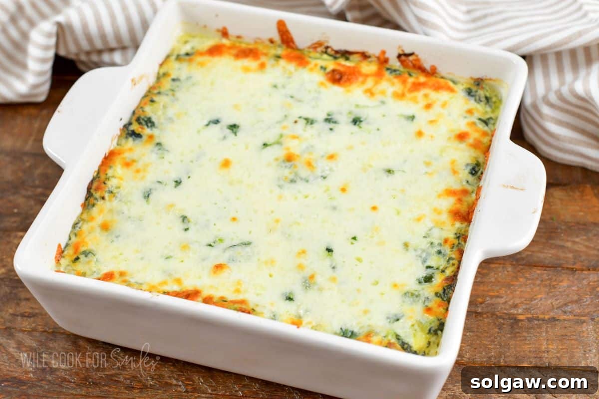 A freshly baked spinach artichoke dip, bubbling around the edges and boasting a perfectly golden brown, melted cheese topping, presented in a white baking dish and ready for immediate serving.