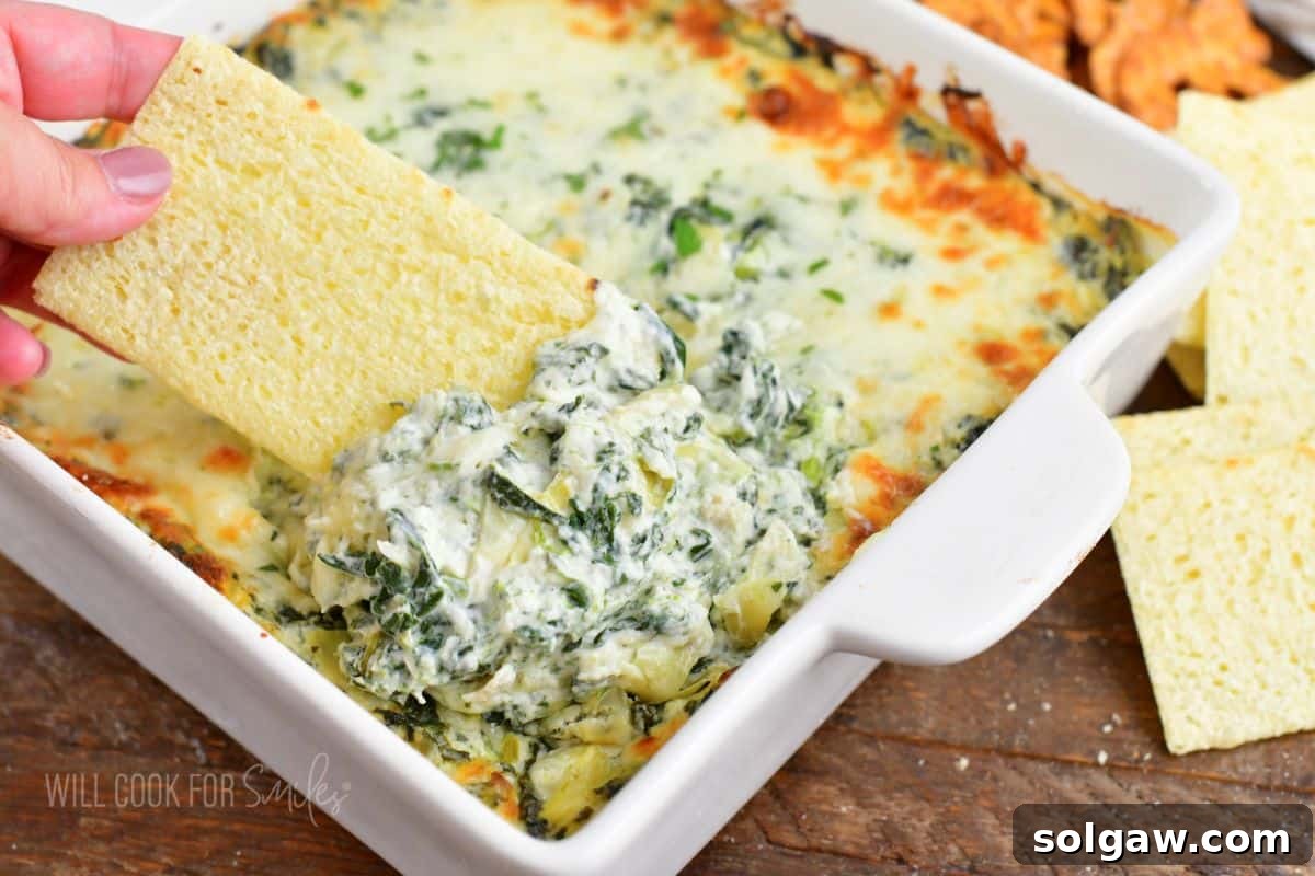 A captivating close-up of a rustic cracker expertly scooping a generous portion of warm, exquisitely cheesy spinach artichoke dip directly from the baking dish, highlighting its creamy texture and melty cheese strands.