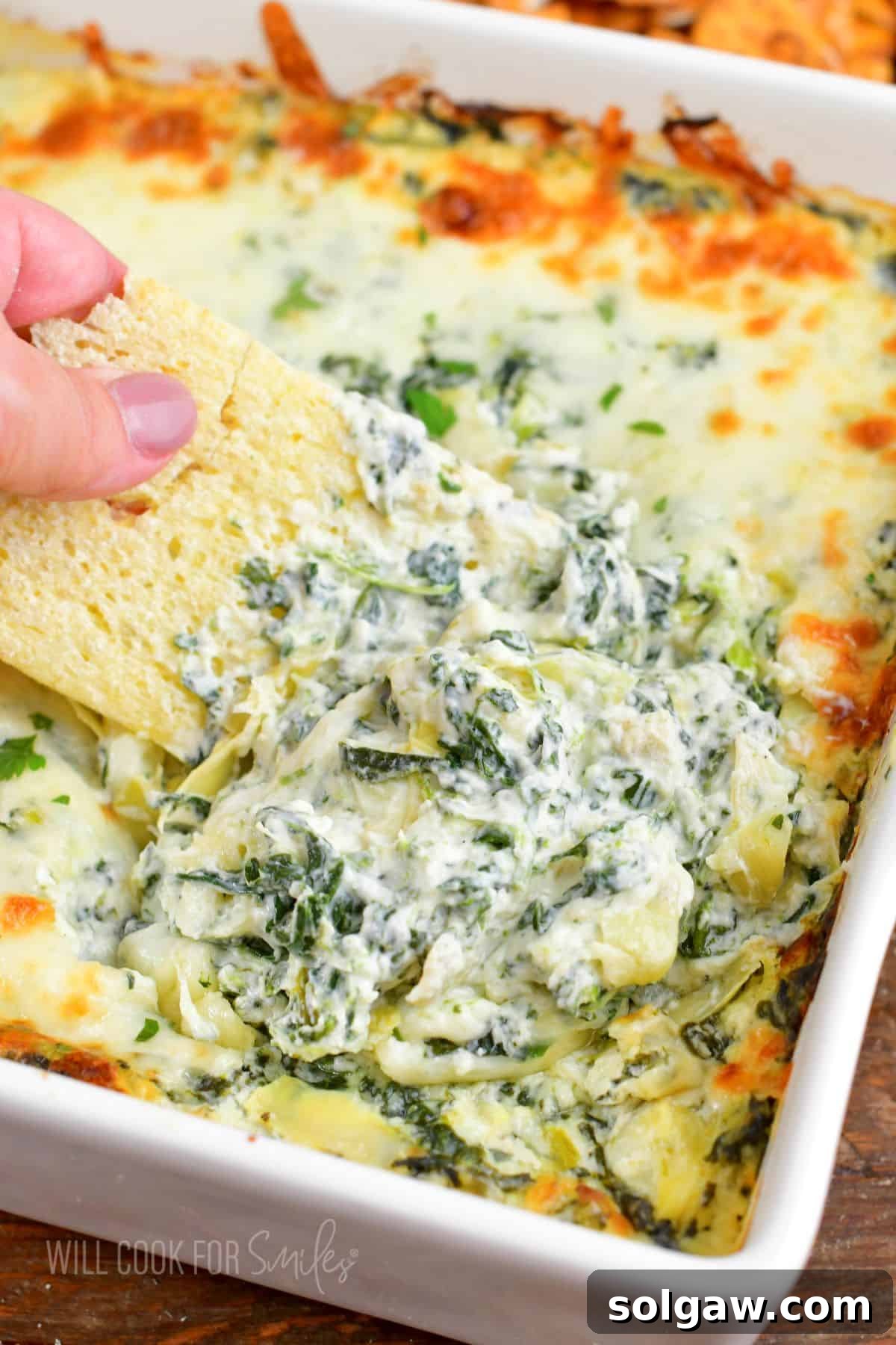 A sturdy serving spoon lifting a generous portion of warm, exquisitely cheesy spinach artichoke dip from the baking dish, with steam gently rising, highlighting its freshness and appeal.
