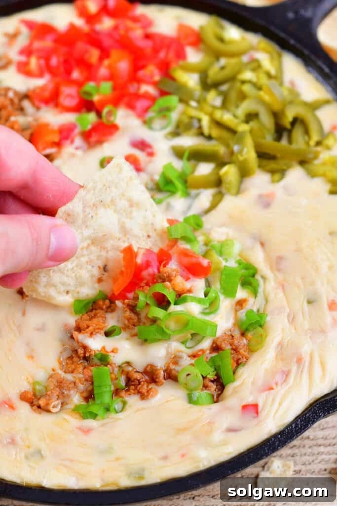 Scooping out some ultimate queso dip with a tortilla chip, showing multiple delicious layers.