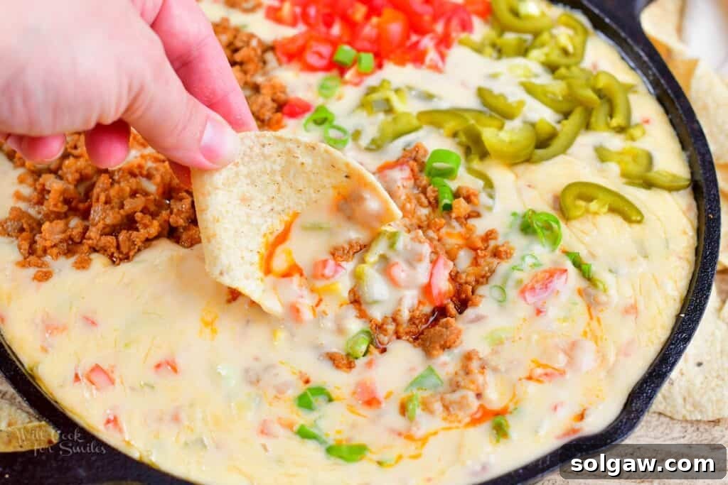 A close-up shot of the ultimate queso dip being scooped with a chip, showing the rich texture and toppings.