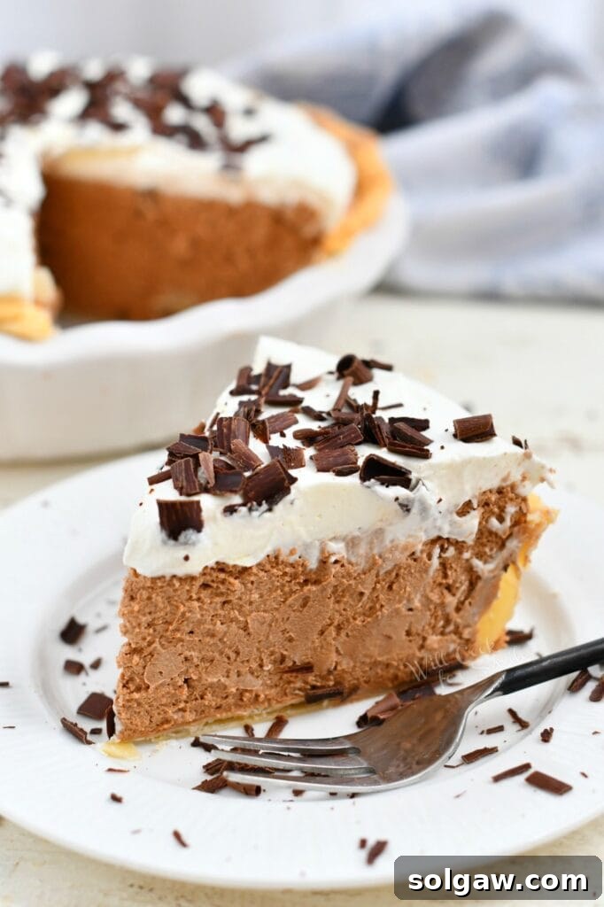 homemade French silk pie on a white plate with fork, showing its silky smooth chocolate filling and whipped cream topping