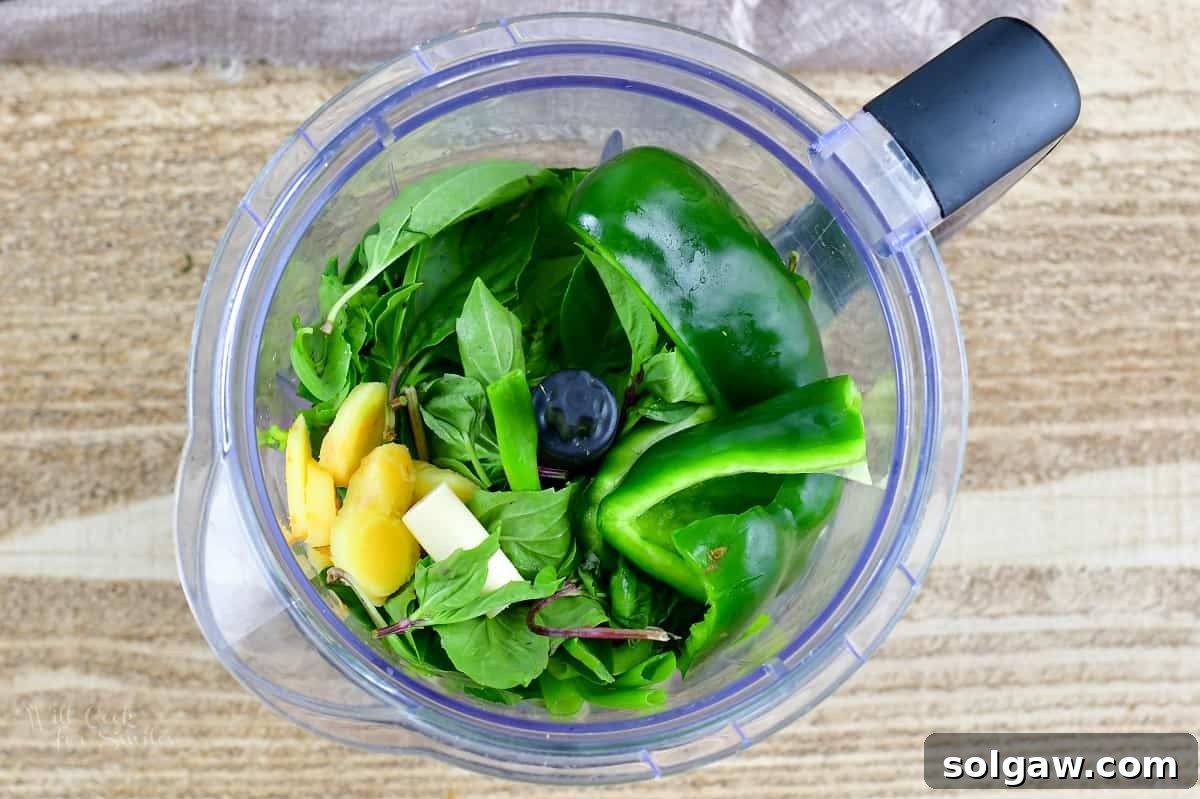 Top-down view of all green curry paste ingredients, roughly chopped, in a blender jar, ready for processing.