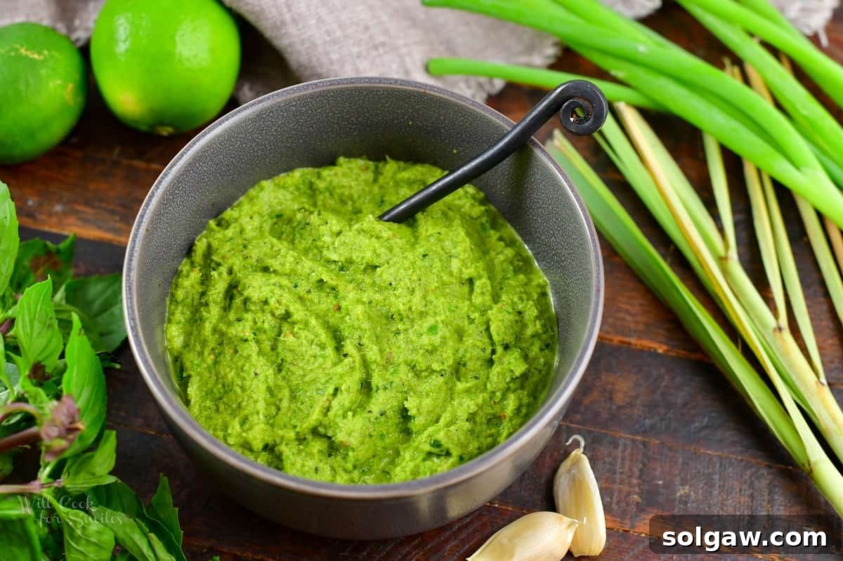 Rich green curry paste presented in a stylish grey bowl with a wooden spoon, showcasing its perfect texture.