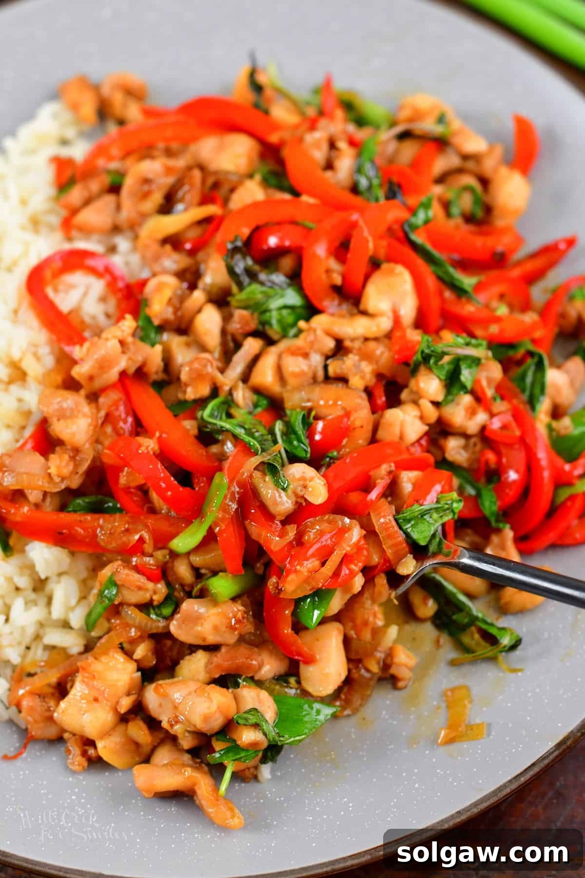 A close-up of a spoon scooping some cooked Thai basil chicken from a wok onto a plate, showcasing the rich colors and textures.