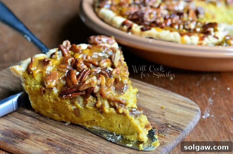 Decadent Pecan Caramel Pumpkin Pie 5 A generous slice of Pecan Caramel Pumpkin Cheesecake Pie on a wooden board, with the whole pie in the background.