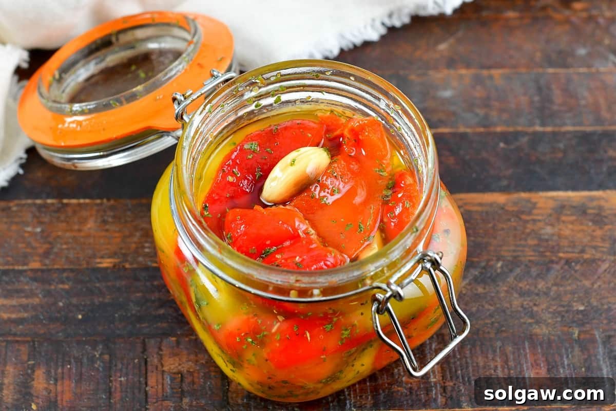 closeup of roasted peppers in oil with garlic and herbs in a jar