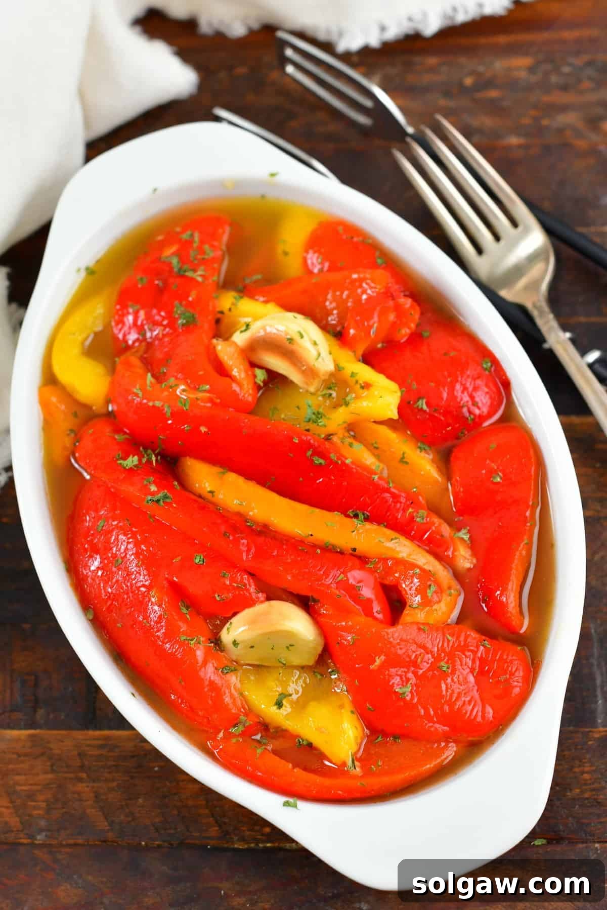 top view of roasted red peppers in oil in a bowl, garnished with fresh herbs