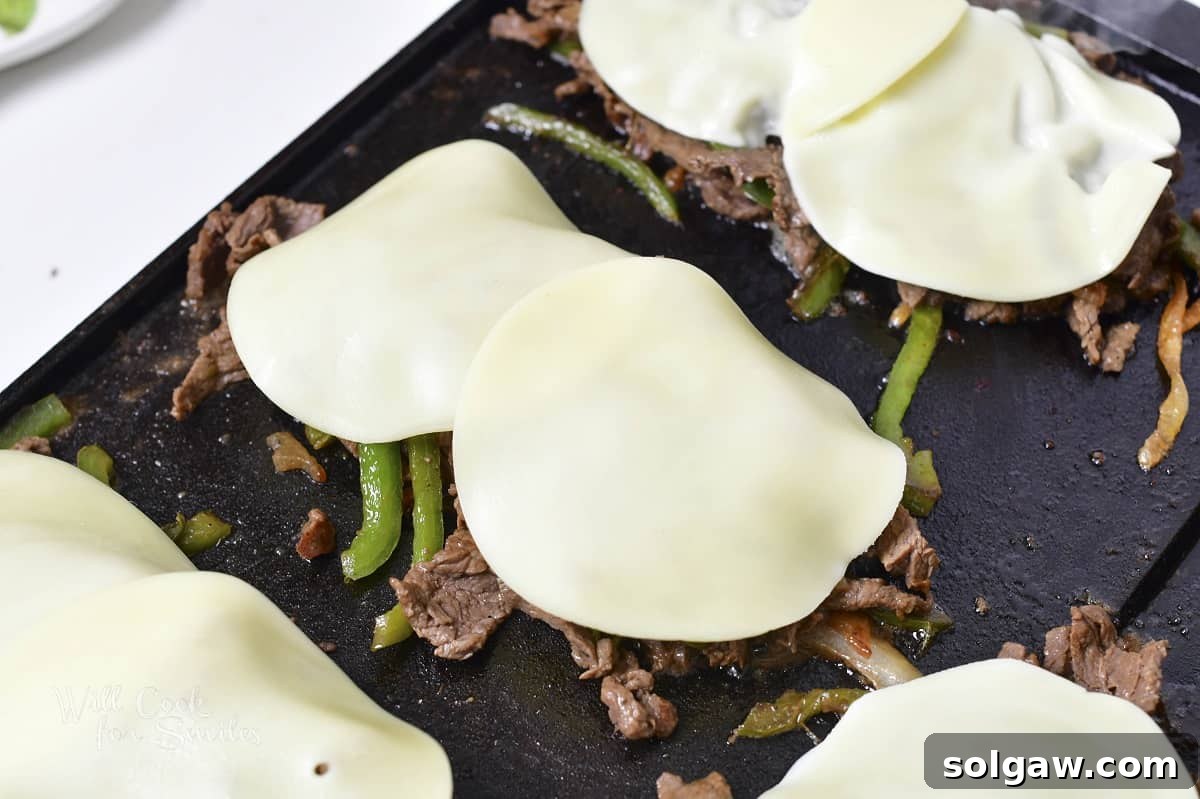 Four mounds of steak, onions, and peppers topped with provolone cheese, melting to perfection on the griddle.