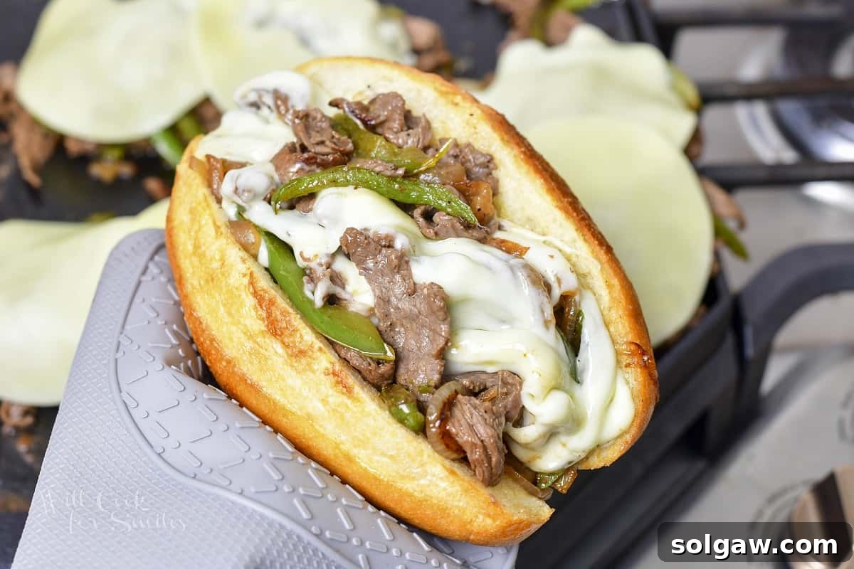 A cheesesteak filling, rich with steak, veggies, and melted cheese, being carefully scooped into a warmed hoagie roll.