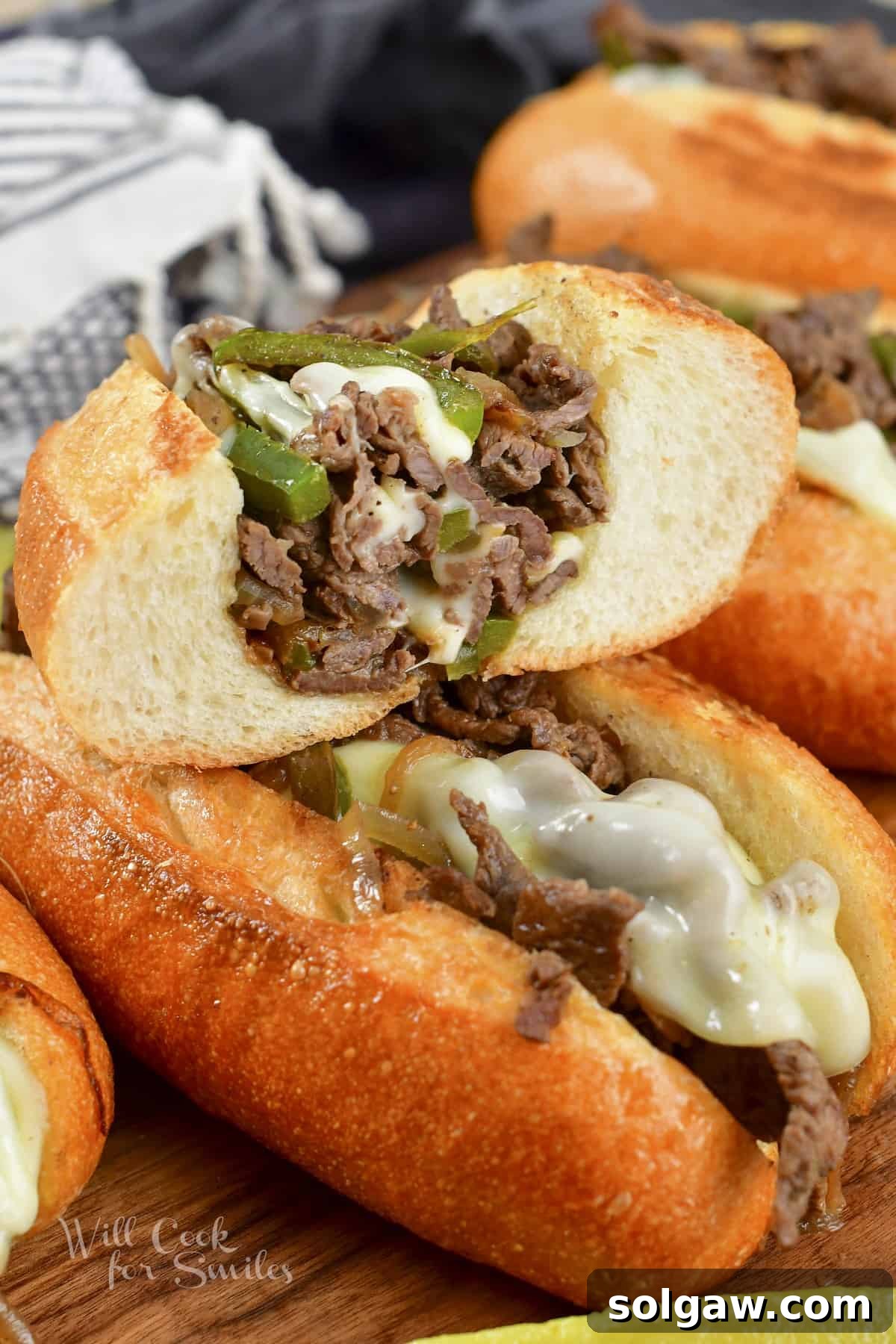 A cross-section of a perfectly cooked Philly Cheesesteak, showing layers of steak, cheese, and vegetables, stacked on another sandwich.