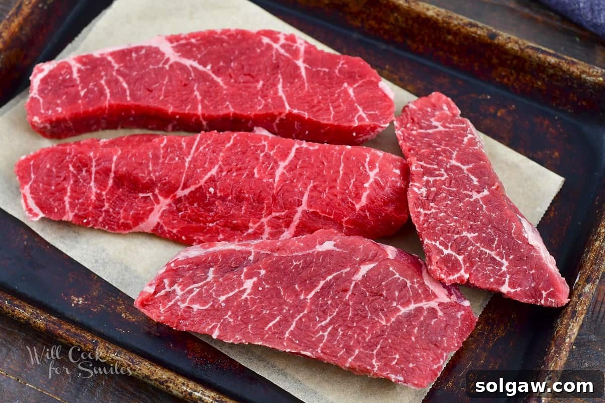 Partially frozen steaks laid out on a baking sheet, prepped for thin slicing.