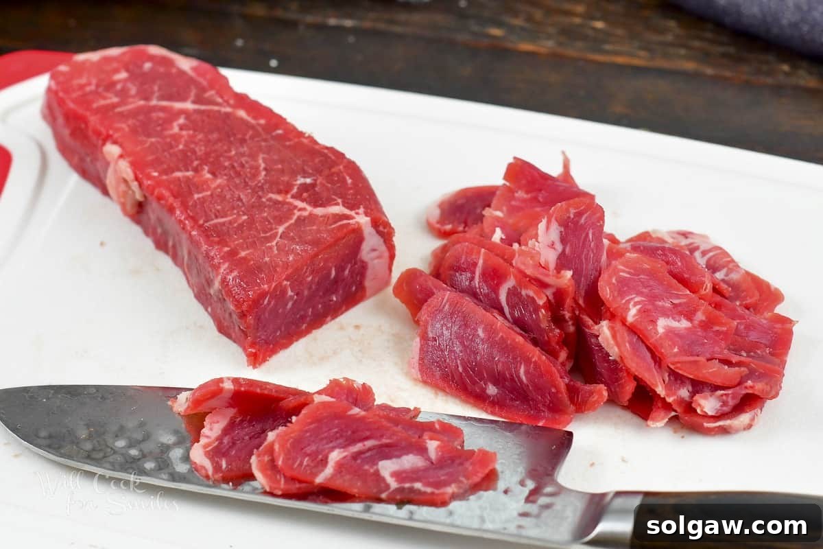 A sharp knife carefully slicing a partially frozen steak into incredibly thin pieces against the grain.