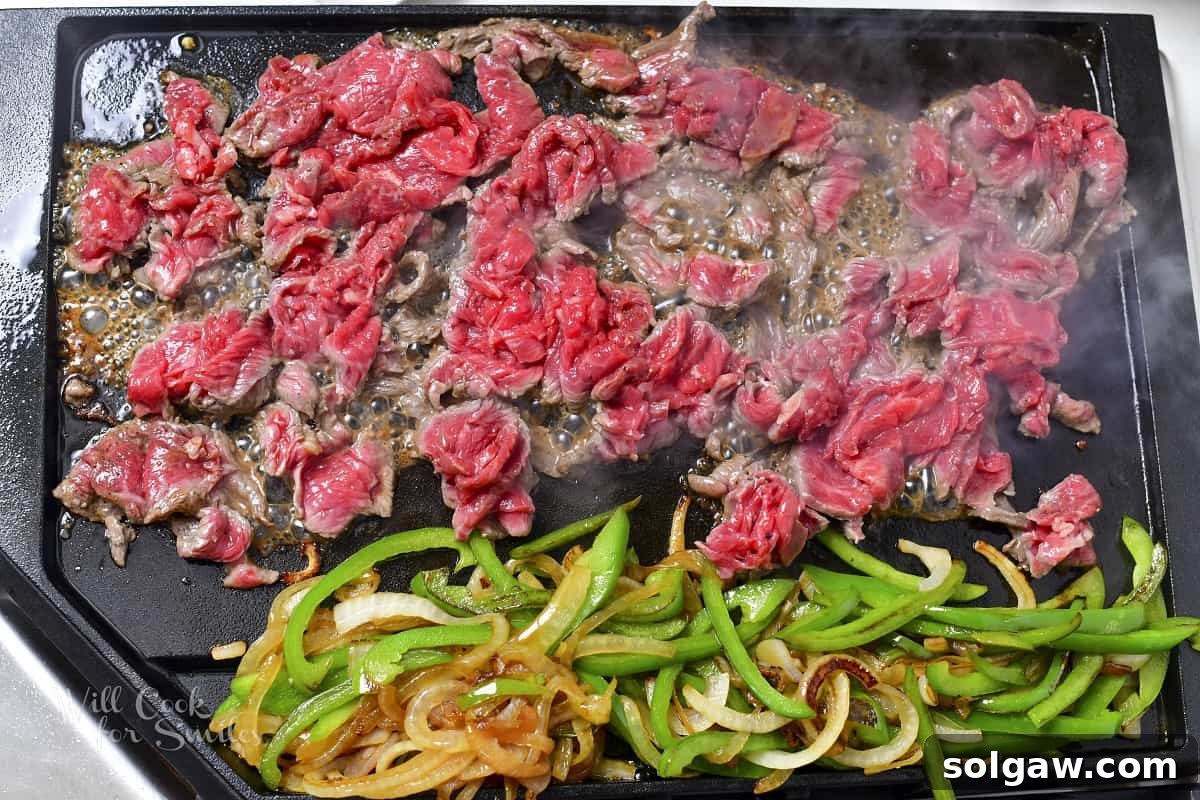 Thinly sliced steak searing next to the onions and peppers on the griddle, ready to be mixed.