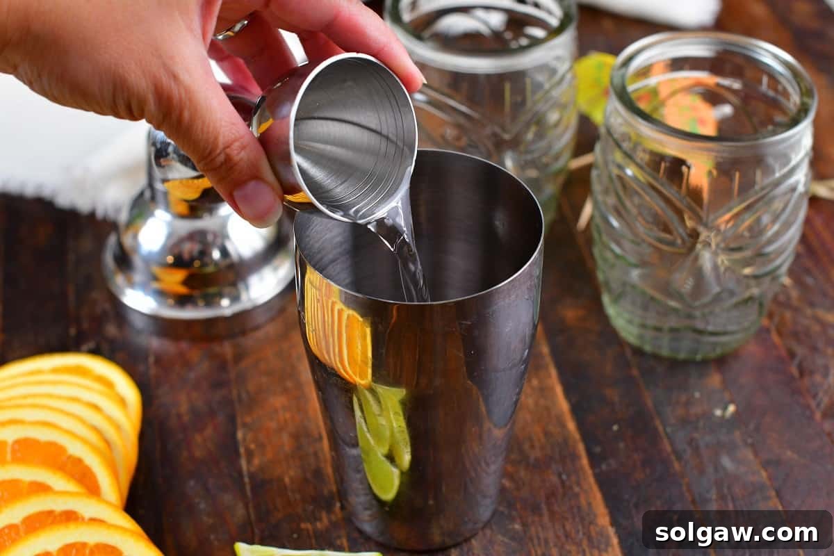 Adding spiced rum to a cocktail shaker filled with ice, preparing for a homemade Calypso Cooler.