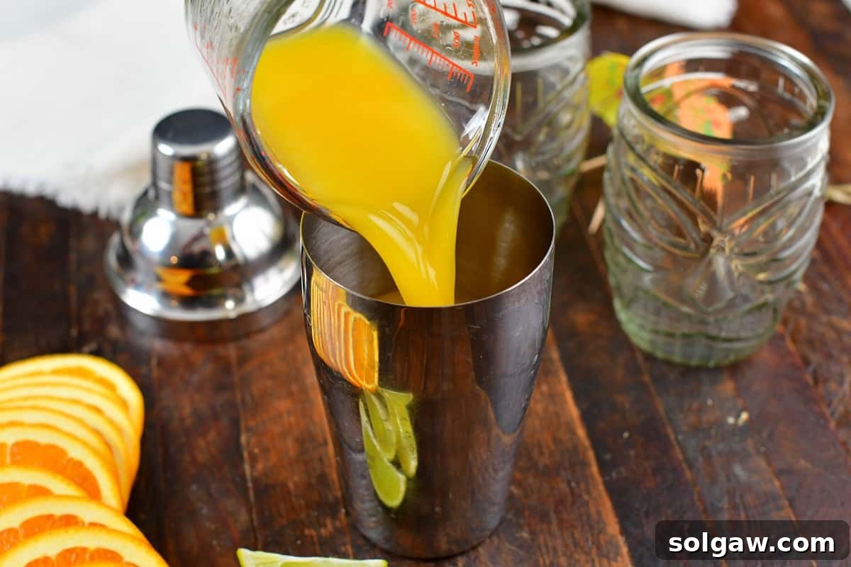 Orange juice being poured into a cocktail shaker, completing the citrus base for the Calypso Cooler.