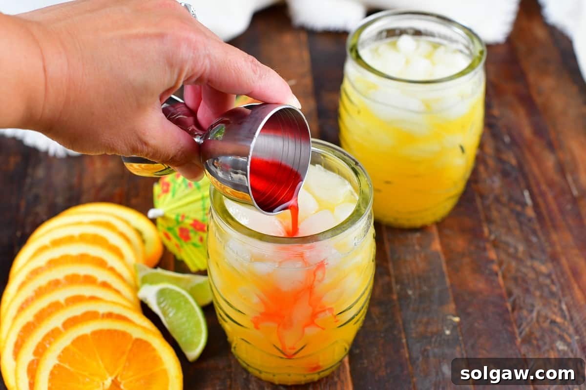 Grenadine being drizzled into the Calypso Cooler, creating a beautiful gradient effect in the glass.
