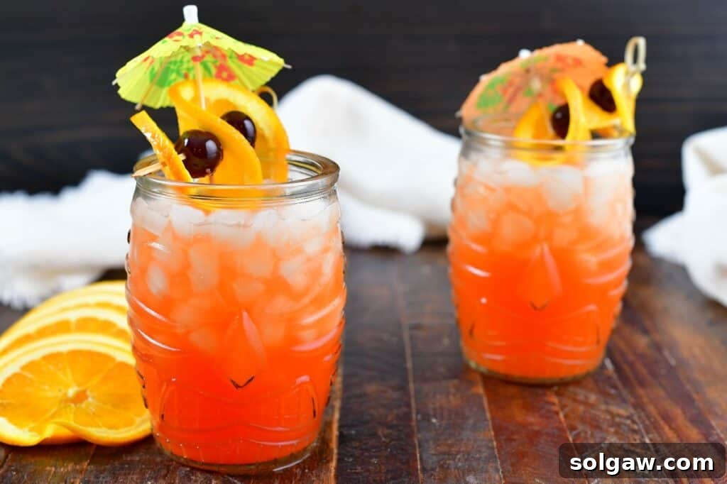 Two perfectly garnished Calypso Cooler rum cocktails in elegant tiki glasses, featuring orange slices and cocktail cherries, ready for a refreshing summer toast.