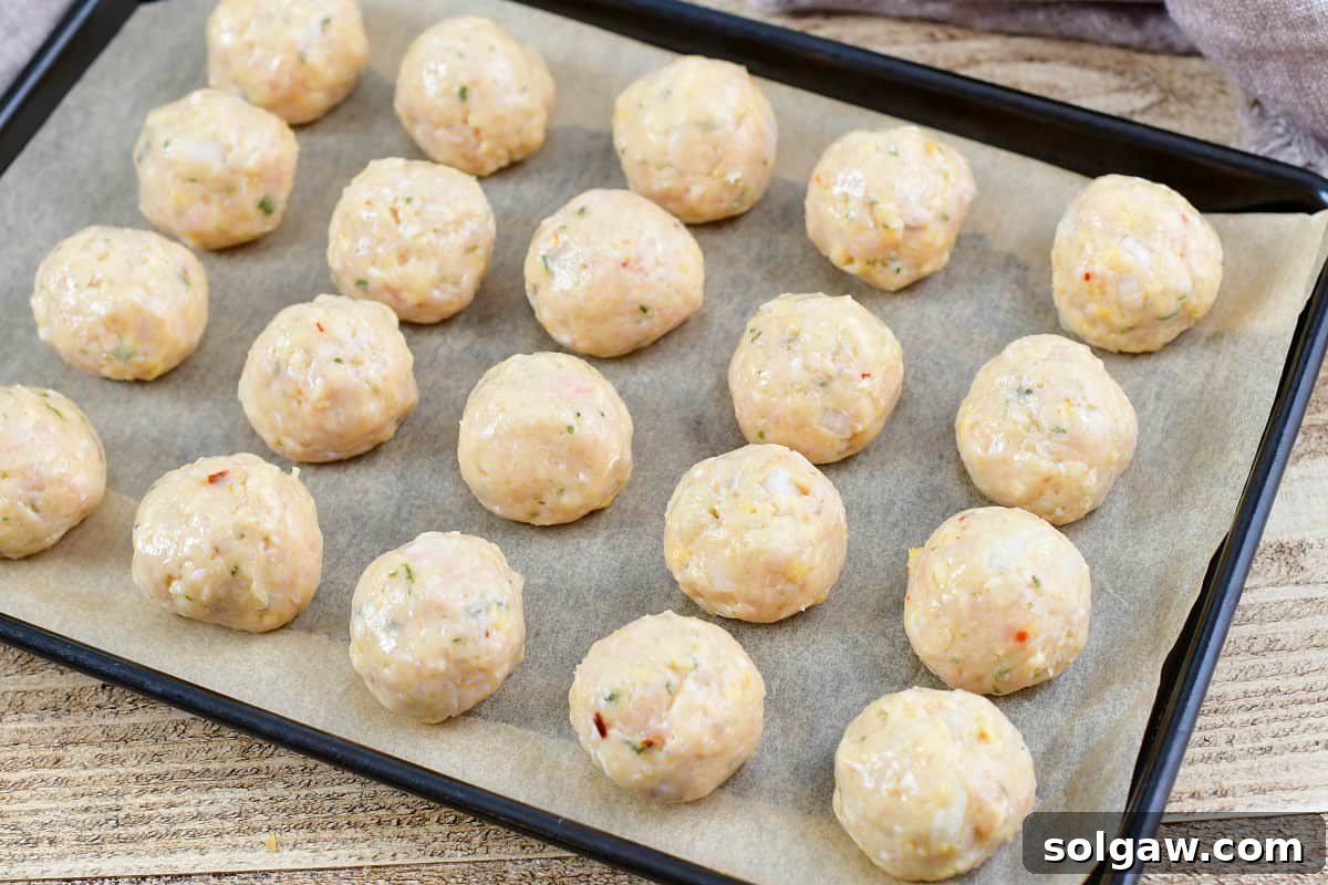 rolled chicken meatballs neatly arranged on a baking sheet, ready for cooking