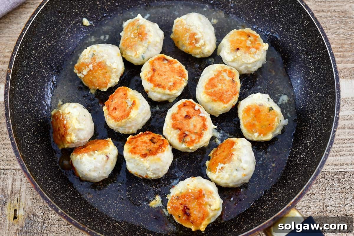 chicken meatballs cooking in a pan, achieving a beautiful sear