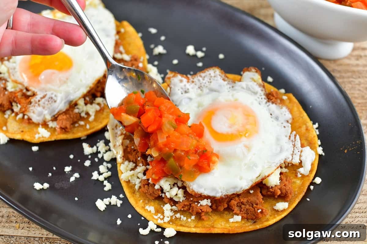 Assembling Huevos Rancheros by spooning the cooked salsa over sunny-side-up eggs, beans, and tortillas.