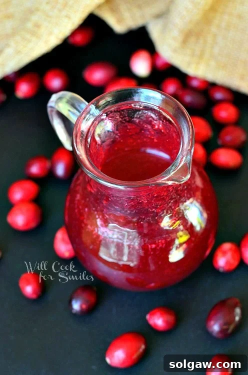 Cranberry Syrup in a glass serving pitcher with cranberries around it