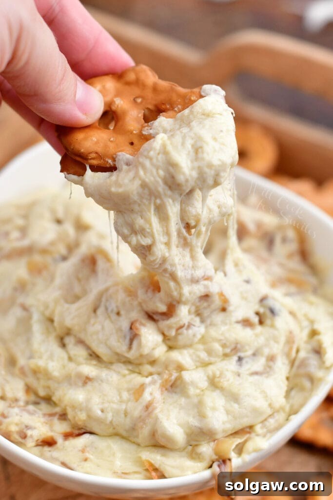 scooping onion dip out of a white bowl with pretzel chips