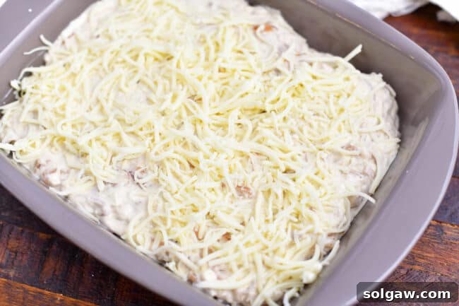 grey baking dish with creamy white mixture topped with white shredded cheese