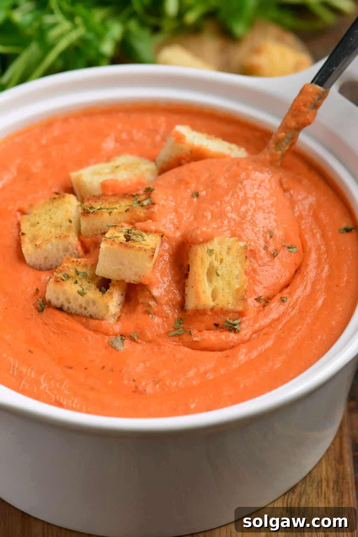 A bowl of rich tomato bisque with a spoonful being lifted, showing its smooth and creamy texture.
