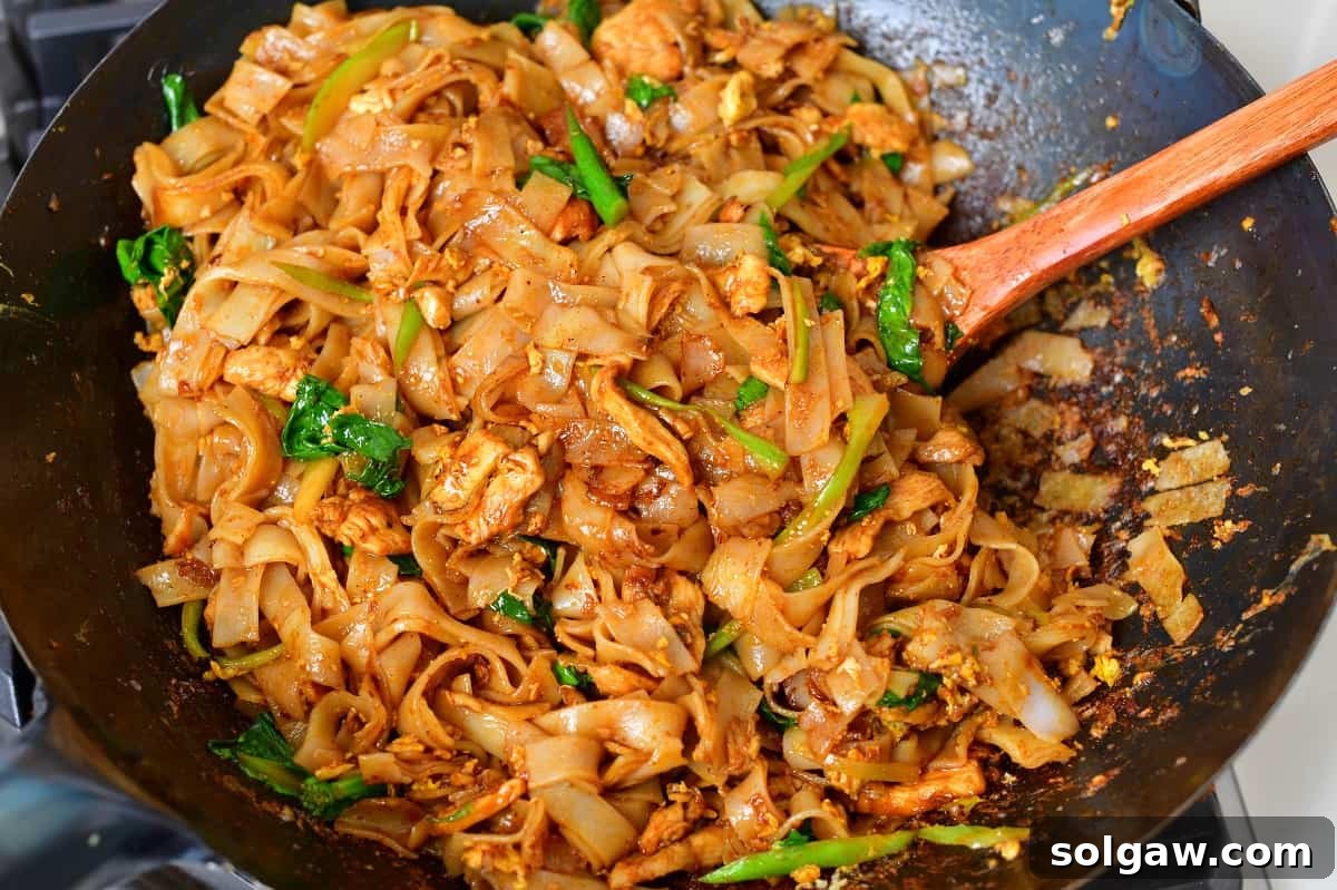 A chef expertly stirring Pad See Ew in a hot wok, illustrating the high-heat cooking technique.