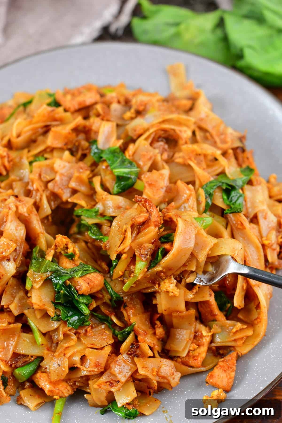 A fork scooping a generous portion of stir-fried noodles from a plate, showing the readiness to enjoy Pad See Ew.