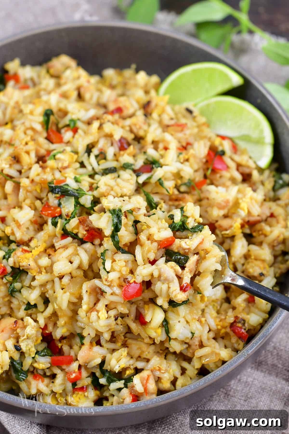 A close-up shot of a fork scooping fragrant Thai Basil Fried Rice from a deep bowl, showcasing the vibrant colors and textures of this popular dish.