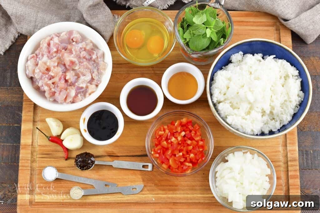 An overhead view of various fresh ingredients laid out on a wooden cutting board, ready to be prepared for Thai Basil Fried Rice, including fresh basil, chili peppers, garlic, onion, and chicken.