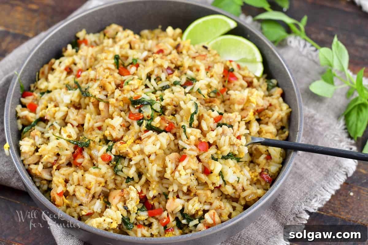 A close-up view of a deep bowl filled with freshly cooked Thai Basil Fried Rice, with a fork digging in, highlighting the tender chicken, vibrant basil, and perfectly coated rice.