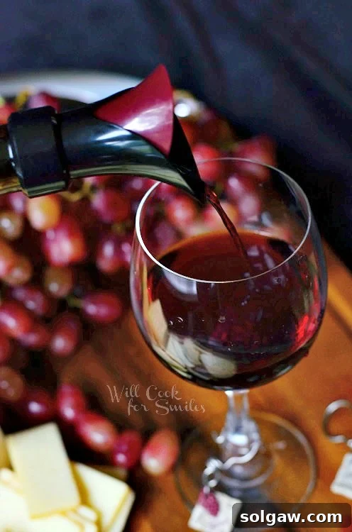 The Art of Wine and Cheese Pairing 5 pouring red wine into a wine glass that is sitting on a cutting board with cheese and grapes