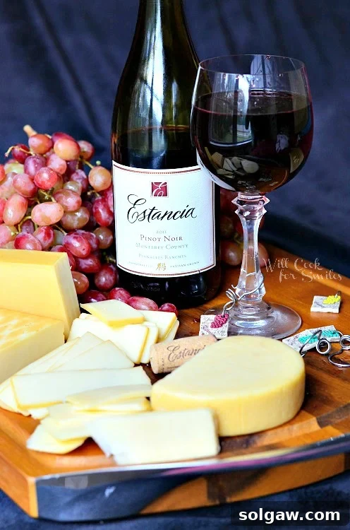 The Art of Wine and Cheese Pairing 6 a glass of red wine with the bottle behind it on a cutting board with cheese and grapes