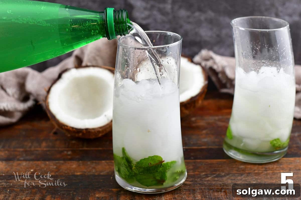 Adding soda water to a glass already filled with ice and the mint and rum mixture.