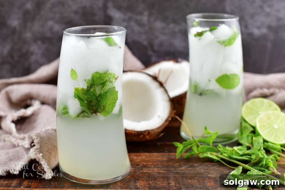 Two white coconut mojito cocktails garnished with mint and lime, with whole coconuts in the background.