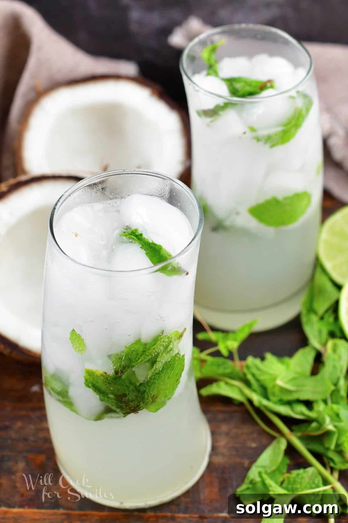 Two glasses filled with white and green coconut mojito cocktails, with a halved coconut and mint sprigs as garnish.
