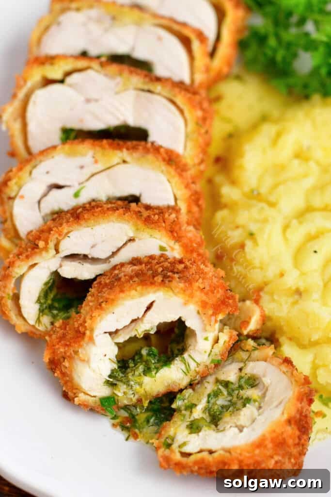 Sliced stuffed chicken breast revealing a vibrant herb butter core, served with a garnish of fresh herbs