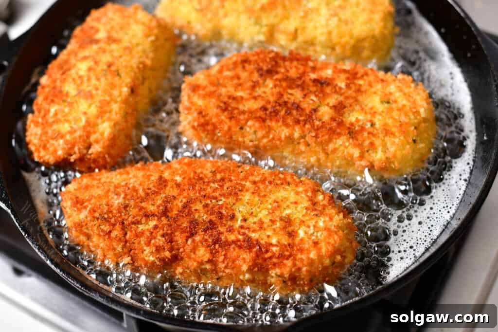 Crispy golden Chicken Kiev cooking in a skillet, showcasing its appealing fried crust.