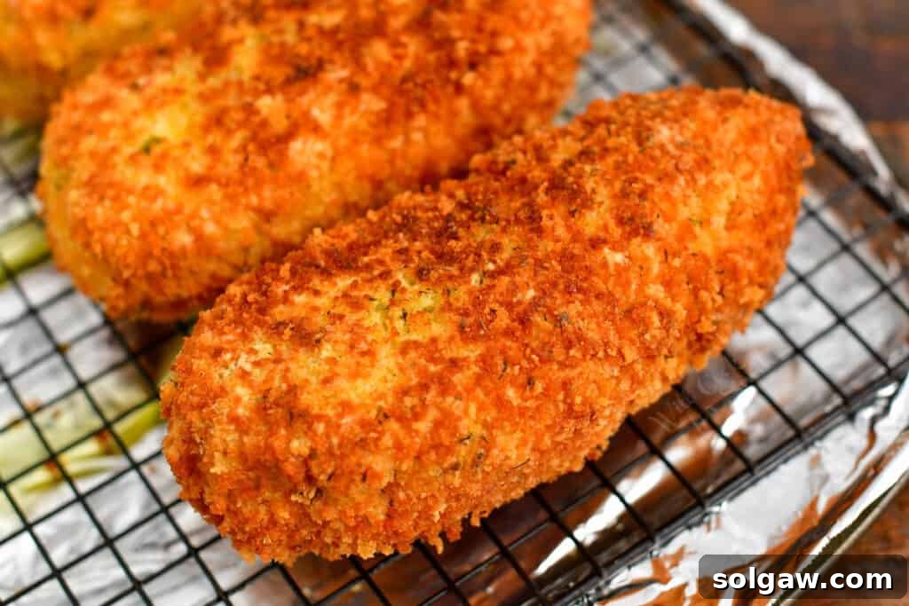 Breaded and fried chicken breast resting on a wire rack over a baking sheet, ready for the oven.