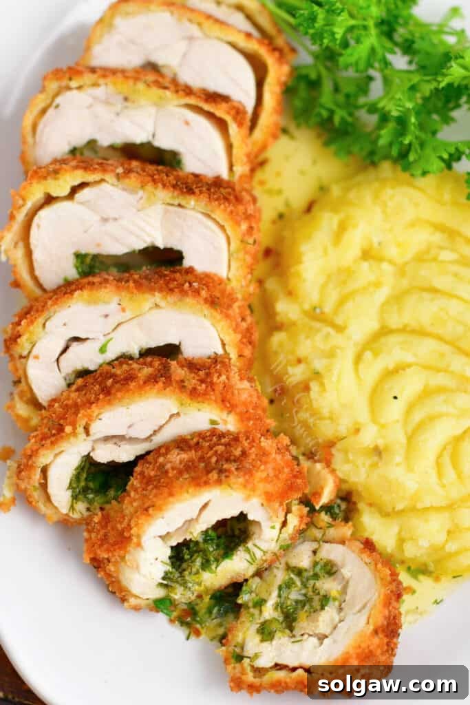 Slices of Chicken Kiev fanned out on a plate, accompanied by creamy whipped potatoes and fresh parsley garnish.