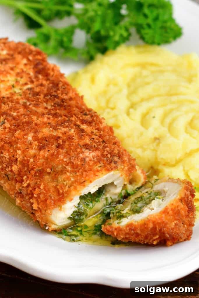 Chicken Kiev served on a bed of whipped potatoes, with one chicken breast cut open to show the melted herb butter inside.