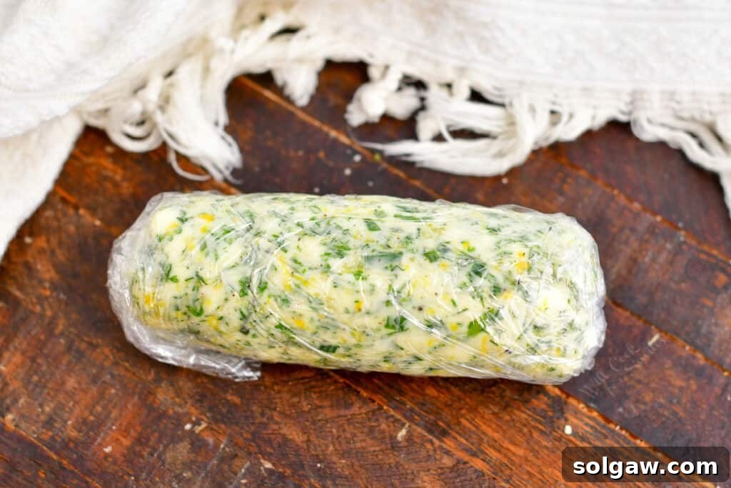 Compound herb butter meticulously rolled into a neat log and wrapped tightly in plastic wrap, ready for chilling.